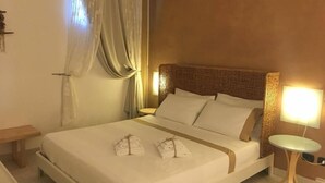 Una habitación de hotel con una cama, una mesita de noche, una lámpara y un ventanal con cortinas.