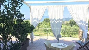 Una terraza con mesa y sillas, plantas en macetas y vistas al campo.