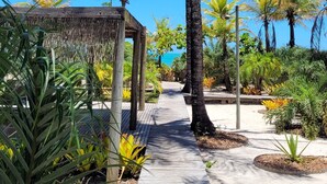 A pathway lined with palm trees and a wooden structure, leading to a beach. - Hotel Vila Naia (Prado)