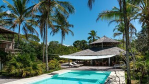 A swimming pool surrounded by palm trees and a covered seating area. - Hotel Vila Naia (Prado)