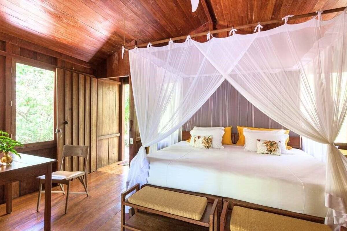 A wooden room with a bed under a white canopy, a wooden desk, and a chair.