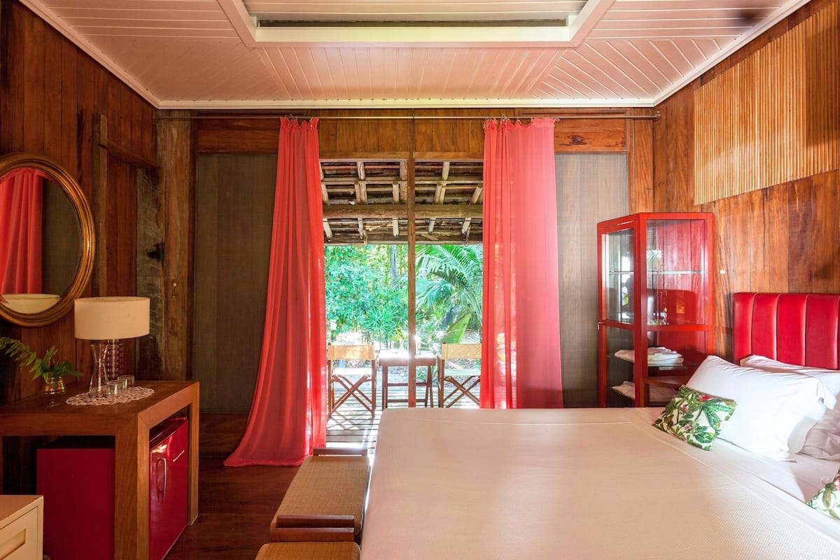 A bedroom with a bed, a desk, a mirror, and a red cabinet.