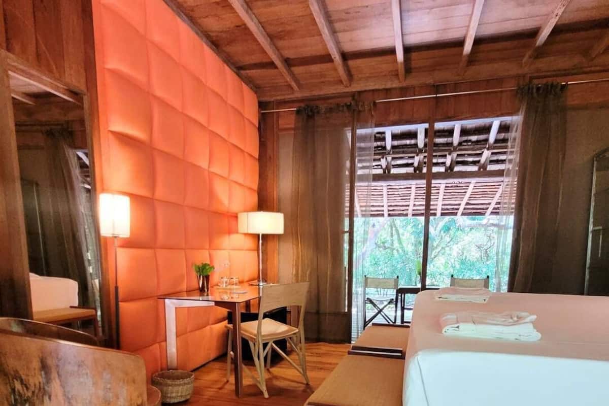 A wooden room with a bed, a table, a chair, and a lamp.