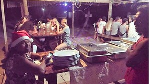 A group of people gathered around tables in a covered outdoor area with string lights. - Cabins in Aguja Island (Narganá)