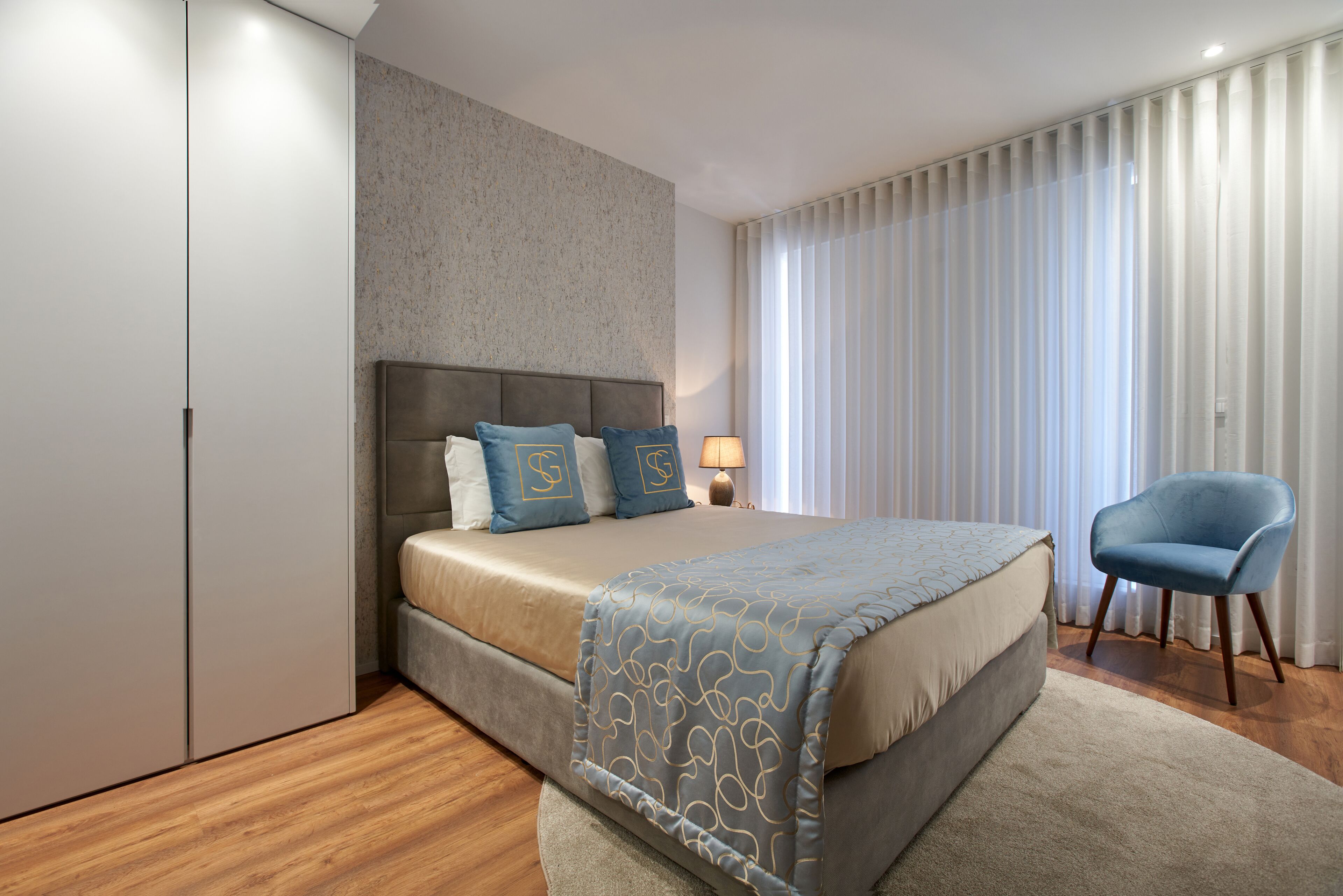 Een moderne slaapkamer met een groot bed, een nachtkastje, een stoel en een kledingkast.