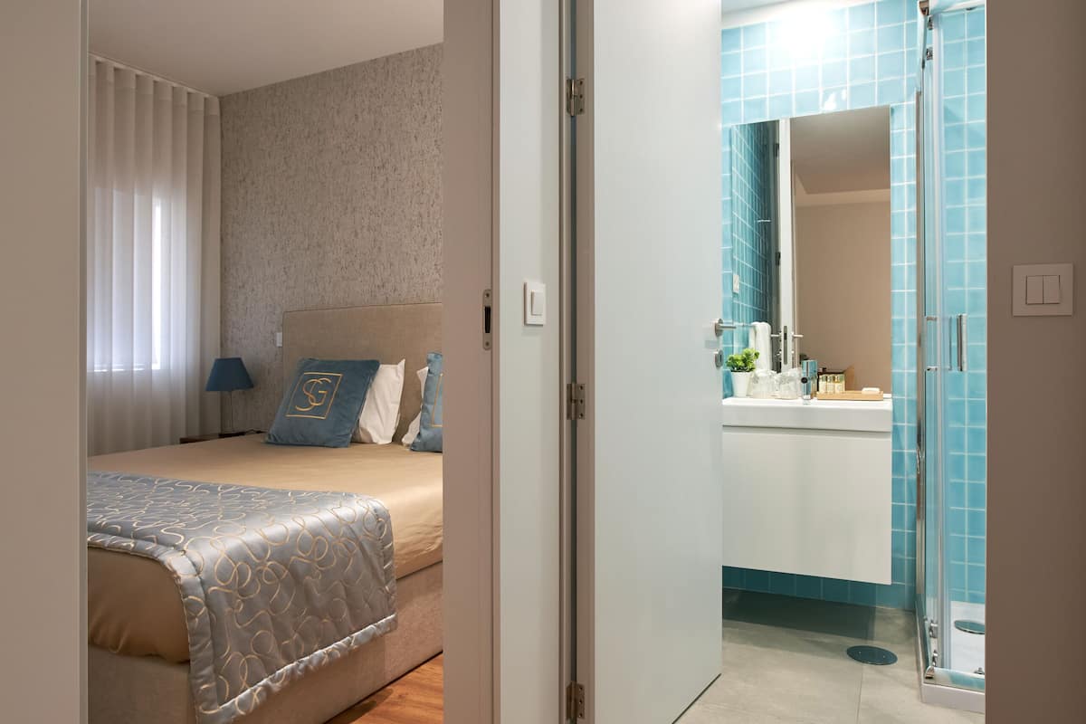 A bedroom with a bed, bedside table, and a bathroom with a sink and mirror.