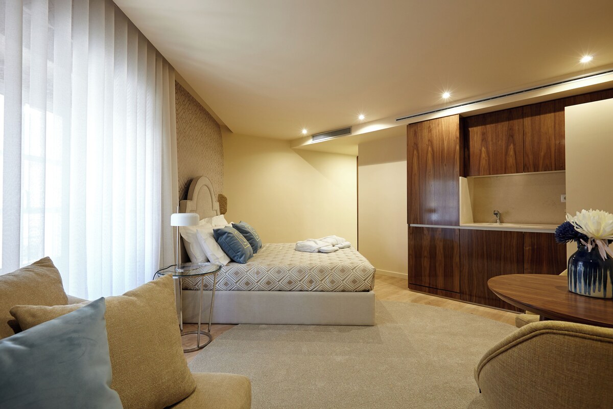 A hotel room with a bed, a sitting area with a sofa, a small table, and a wooden cabinet.