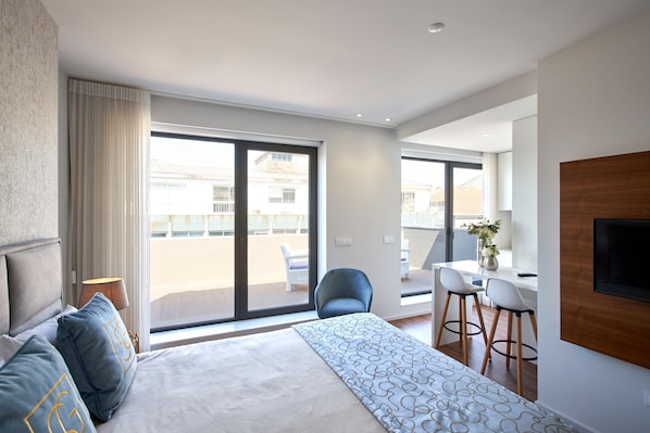 Une chambre d’hôtel moderne dotée d’un grand lit, d’un balcon avec vue, d’un coin repas avec deux chaises et d’un téléviseur fixé au mur.