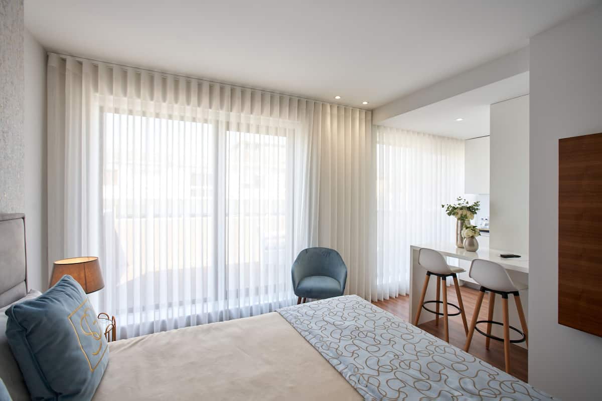 A modern hotel room with a large bed, a desk with two chairs, and a large window with sheer curtains.