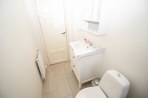 A small, white bathroom with a toilet, sink, and a mirror above the sink. - Seafarer Court - Warm and Cozy Apartment (Reykjavik)