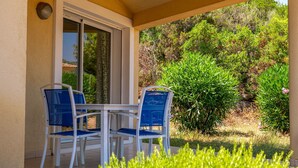 An outdoor patio with a table and two chairs, surrounded by greenery and a view of the landscape. - Résidence Odalys San Martinu (Zonza)