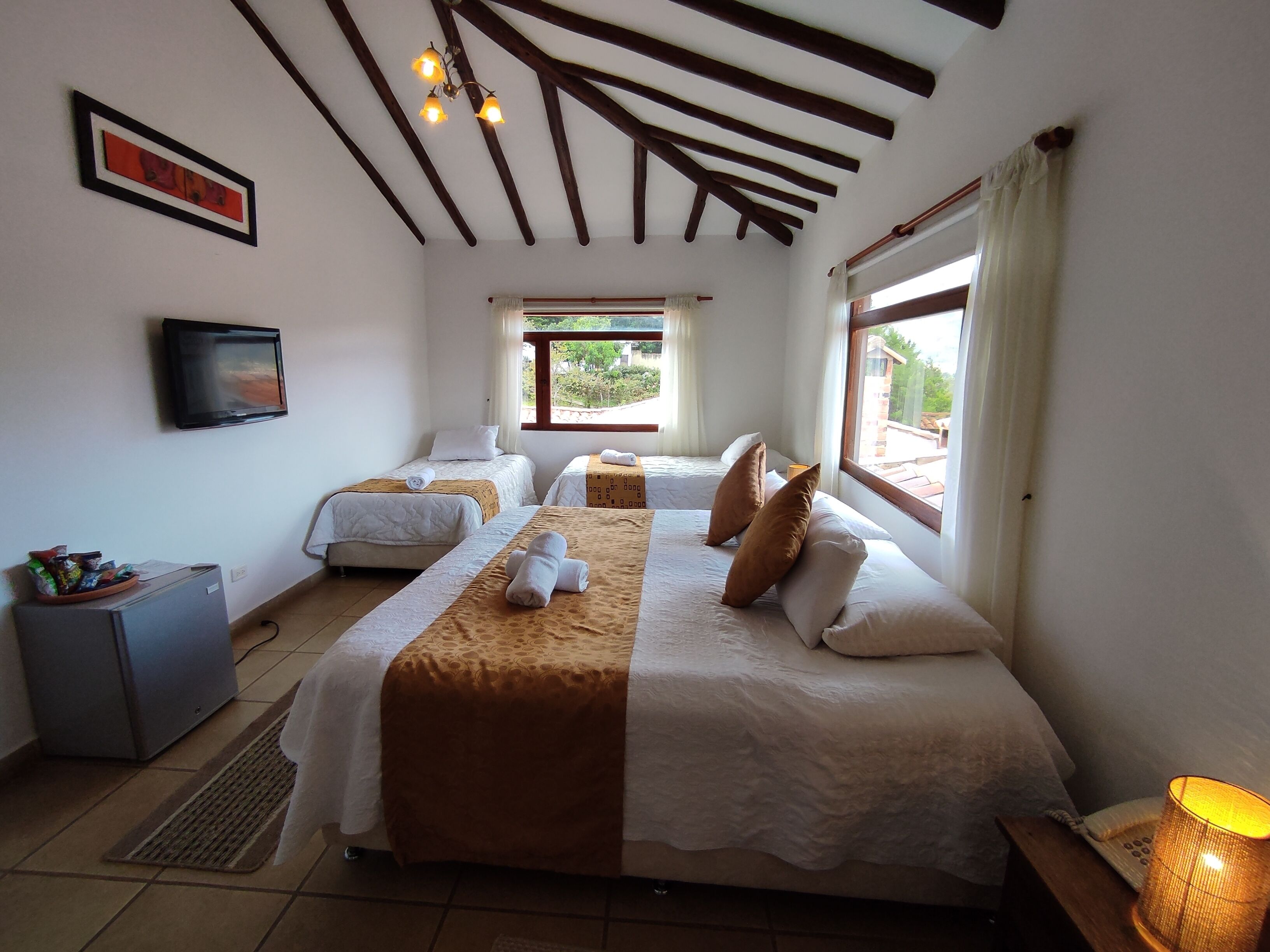 A hotel room with two beds, a television, a small desk, and a window with a view of greenery.