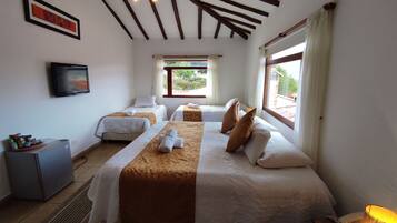 A hotel room with two beds, a television, a small desk, and a window with a view of greenery.