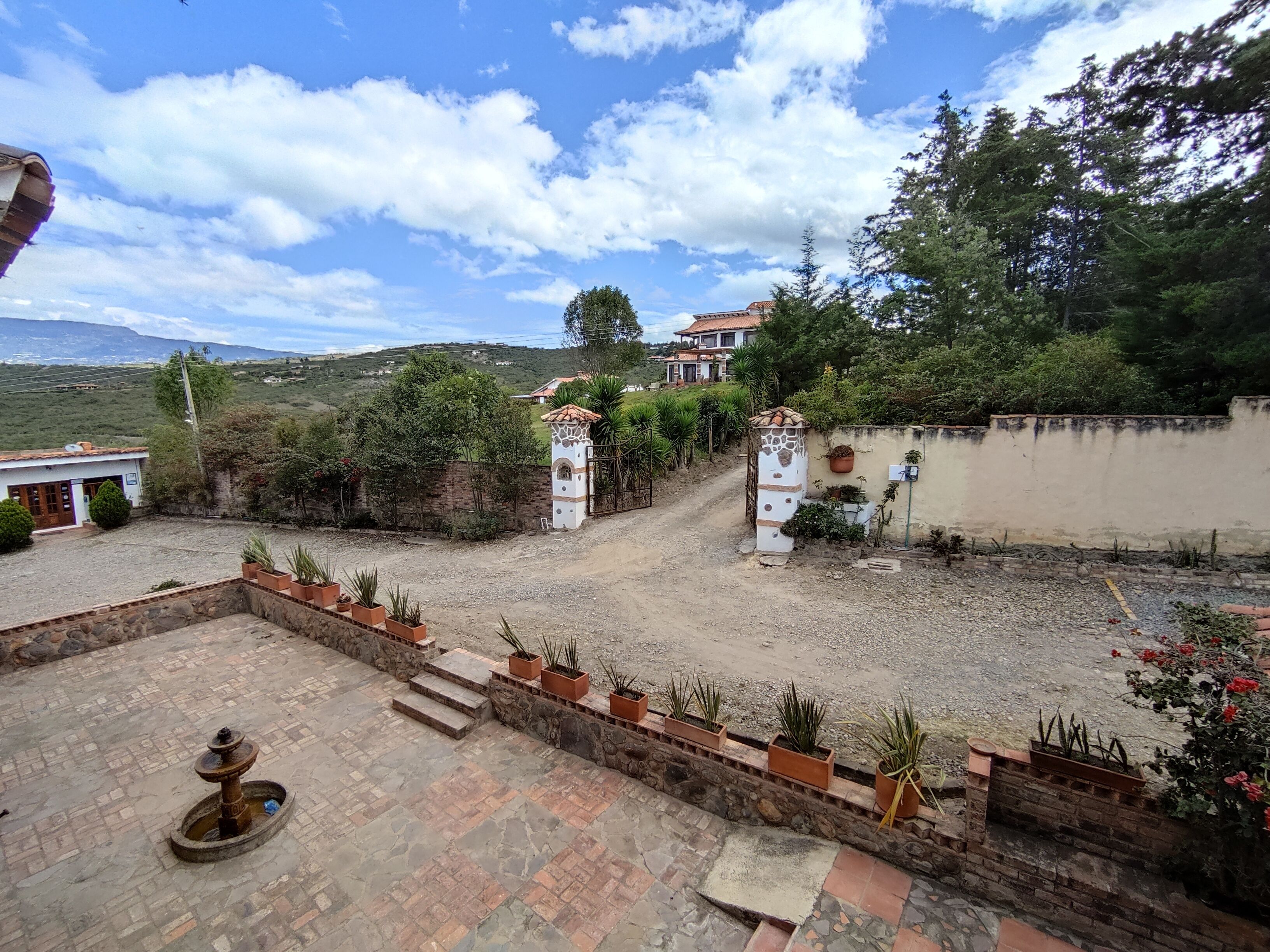 Un patio con una fuente, plantas en macetas y un muro de piedra.