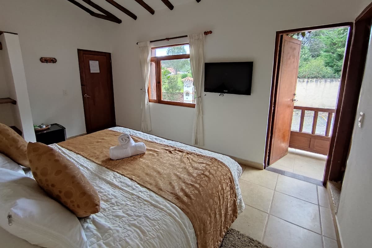 Une chambre à coucher avec un lit, une télévision, une fenêtre avec des rideaux et une porte ouverte donnant sur l’extérieur.