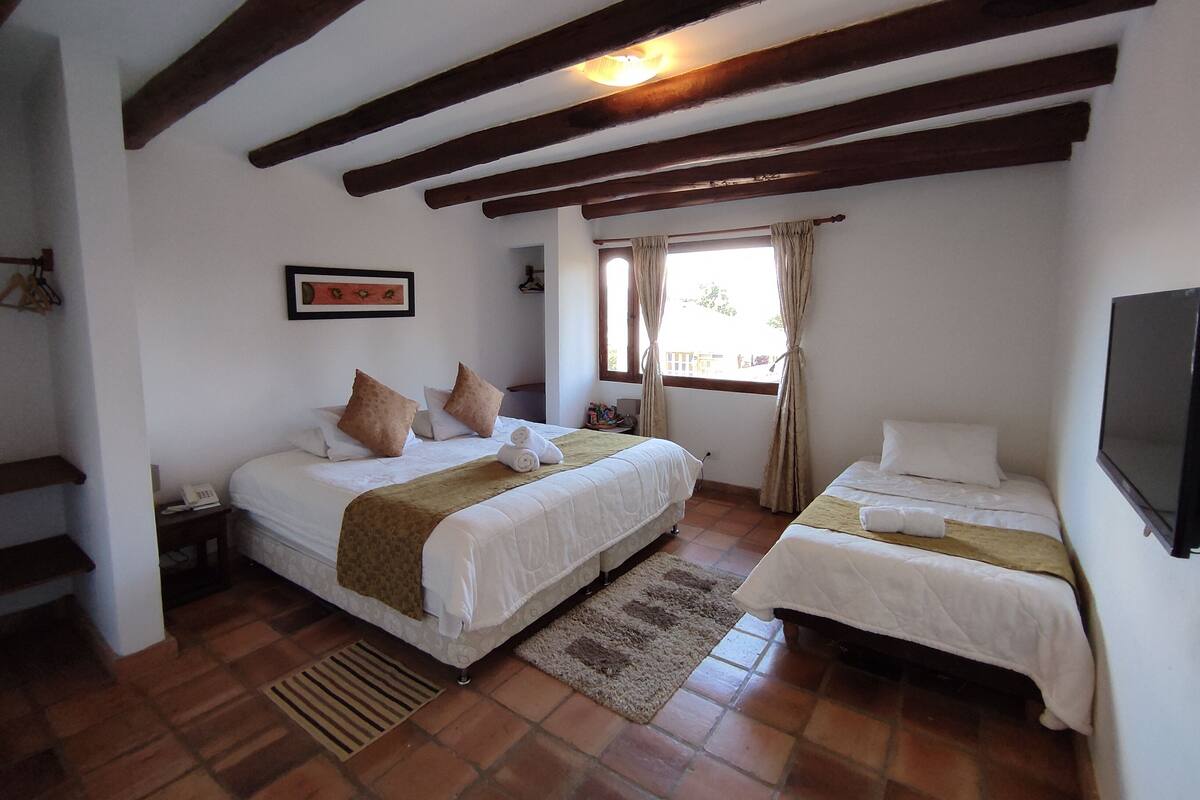 Une chambre avec deux lits, un plafond en bois, une fenêtre avec des rideaux, un tableau encadré au mur et un téléviseur fixé au mur.