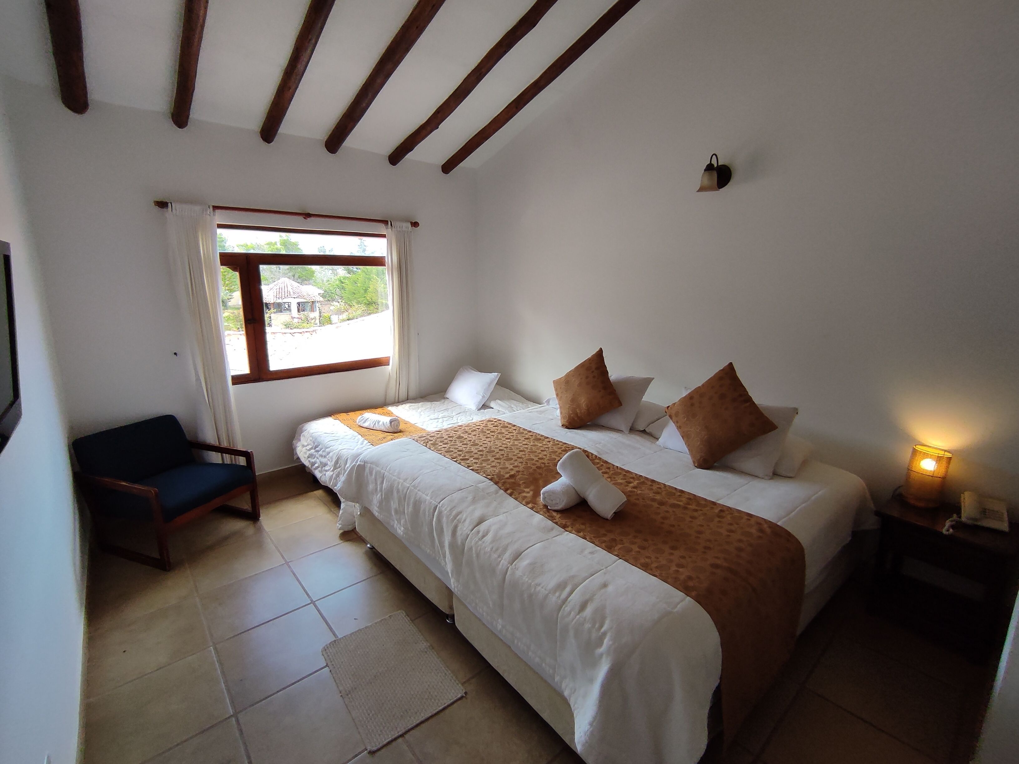 Una camera da letto con due letti, una finestra con tende, una sedia e una lampada da comodino.