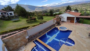 Un patio trasero con piscina, un muro de piedra y vistas a montañas lejanas.