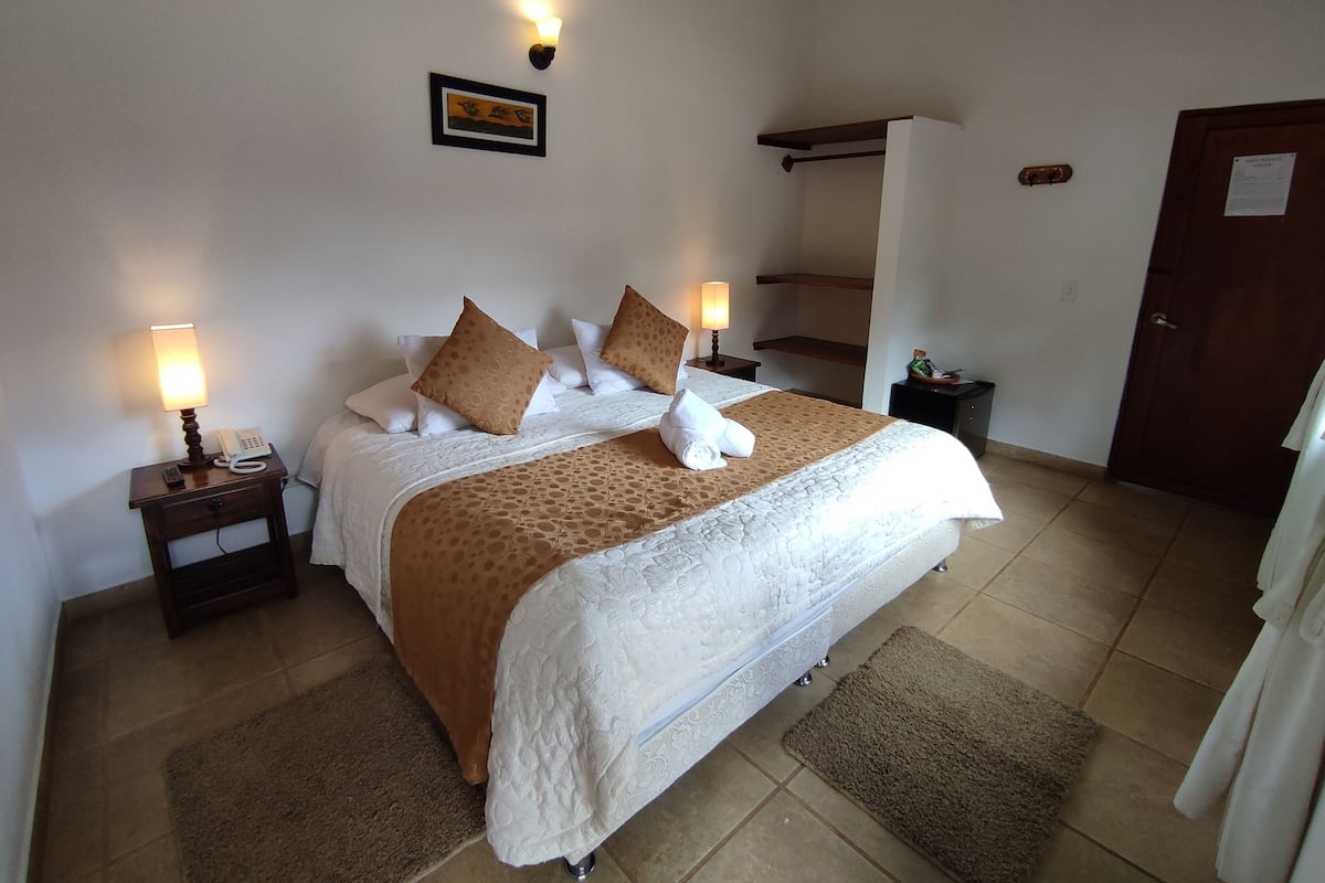 Une chambre à coucher bien rangée, avec un lit, des lampes de chevet, une petite table avec un téléphone, un tableau encadré au mur et une porte avec une serrure.