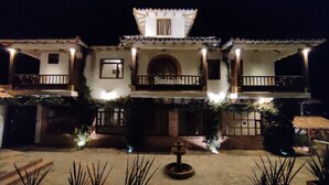Un edificio de dos pisos con un balcón, un letrero que dice "Bienvenidos" y una fuente en el patio.