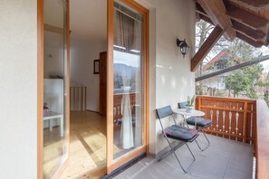 Un balcone con ringhiera in legno, un tavolo con sedie e una porta scorrevole in vetro che dà su un ambiente interno.