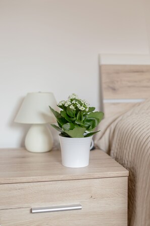Un comodino in legno con una lampada bianca e una pianta in vaso.