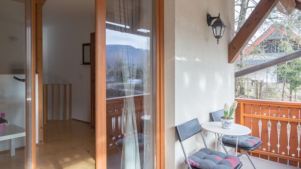 Un balcón con suelo de madera, puerta de cristal y una pequeña mesa con sillas.