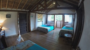 Una habitación rústica con pisos de madera y techo inclinado, con dos camas con ropa de cama azul y una mesita pequeña.