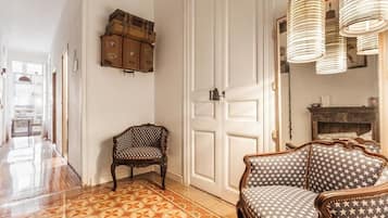 Een kamer met patroon vloertegels, een houten kast met koffers, een gestreept bankje en een deur met spiegel.