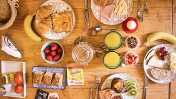 Een houten tafel met ontbijtproducten zoals brood, fruit, eieren en drankjes.