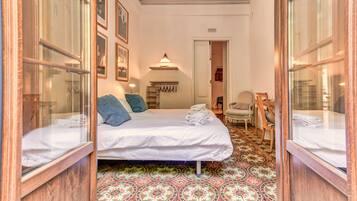 Habitación de hotel con cama, una silla, una mesita, estante en la pared y suelo estampado.