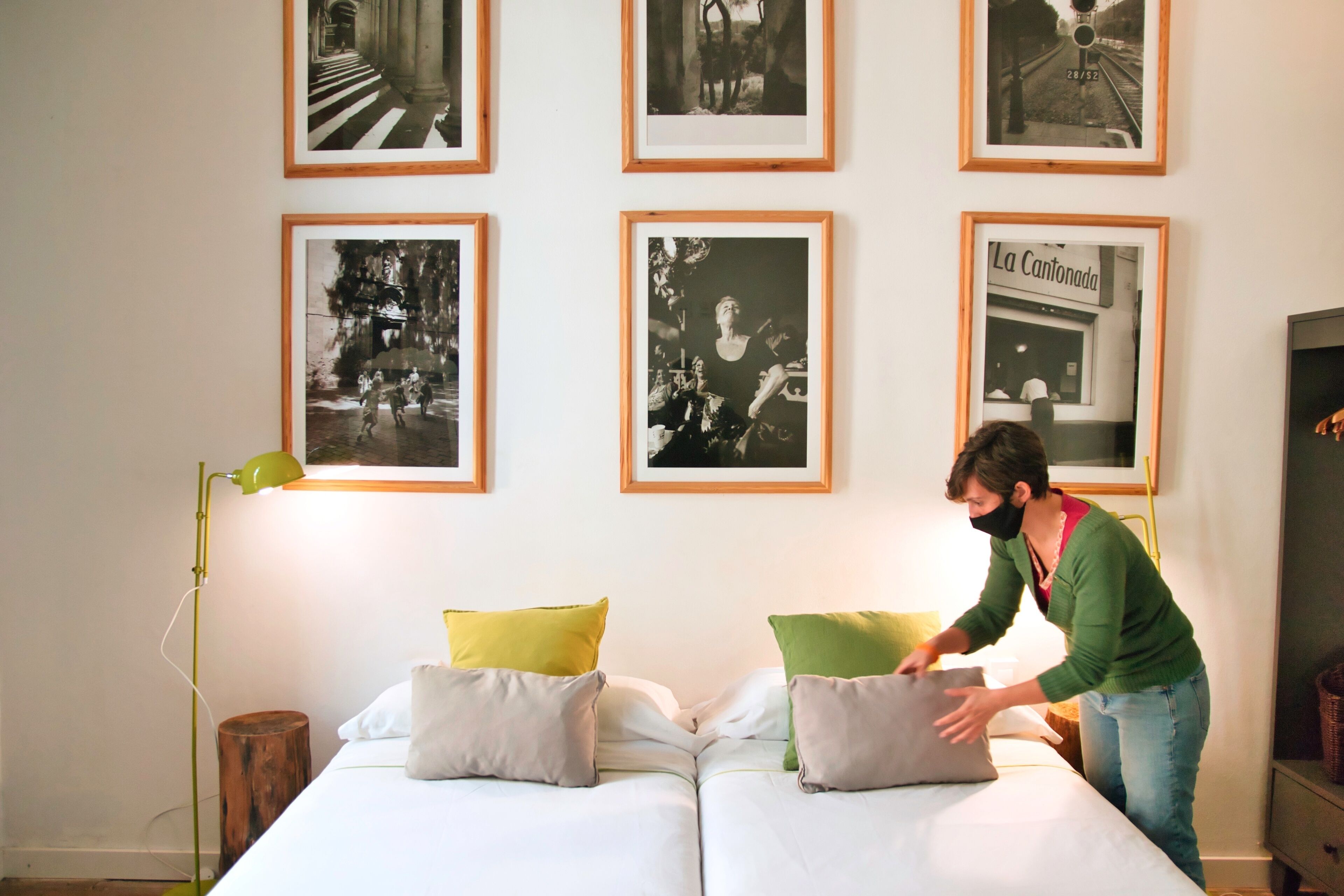 Una habitación con dos camas, una lámpara de pie verde y fotografías enmarcadas en blanco y negro en la pared.