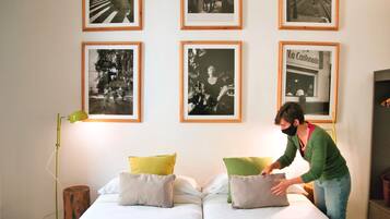 Una habitación con dos camas, una lámpara de pie verde y fotografías enmarcadas en blanco y negro en la pared.