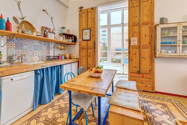 A kitchen with a wooden table, blue chairs, a blue curtain, and a patterned floor.