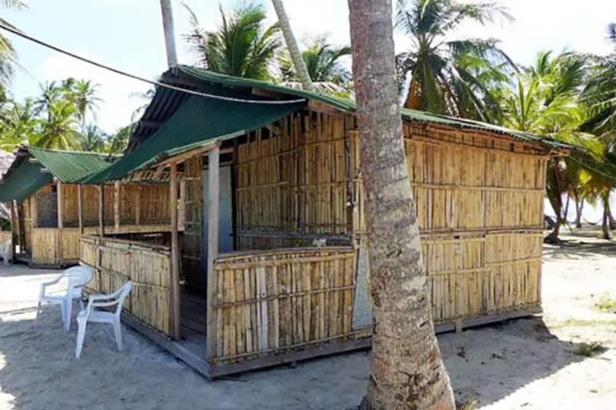 A small, single-story bamboo structure with a green awning, a small porch area, and a few plastic chairs outside.