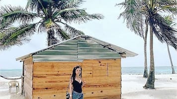 Una cabaña de madera en la playa, con palmeras y el océano al fondo.