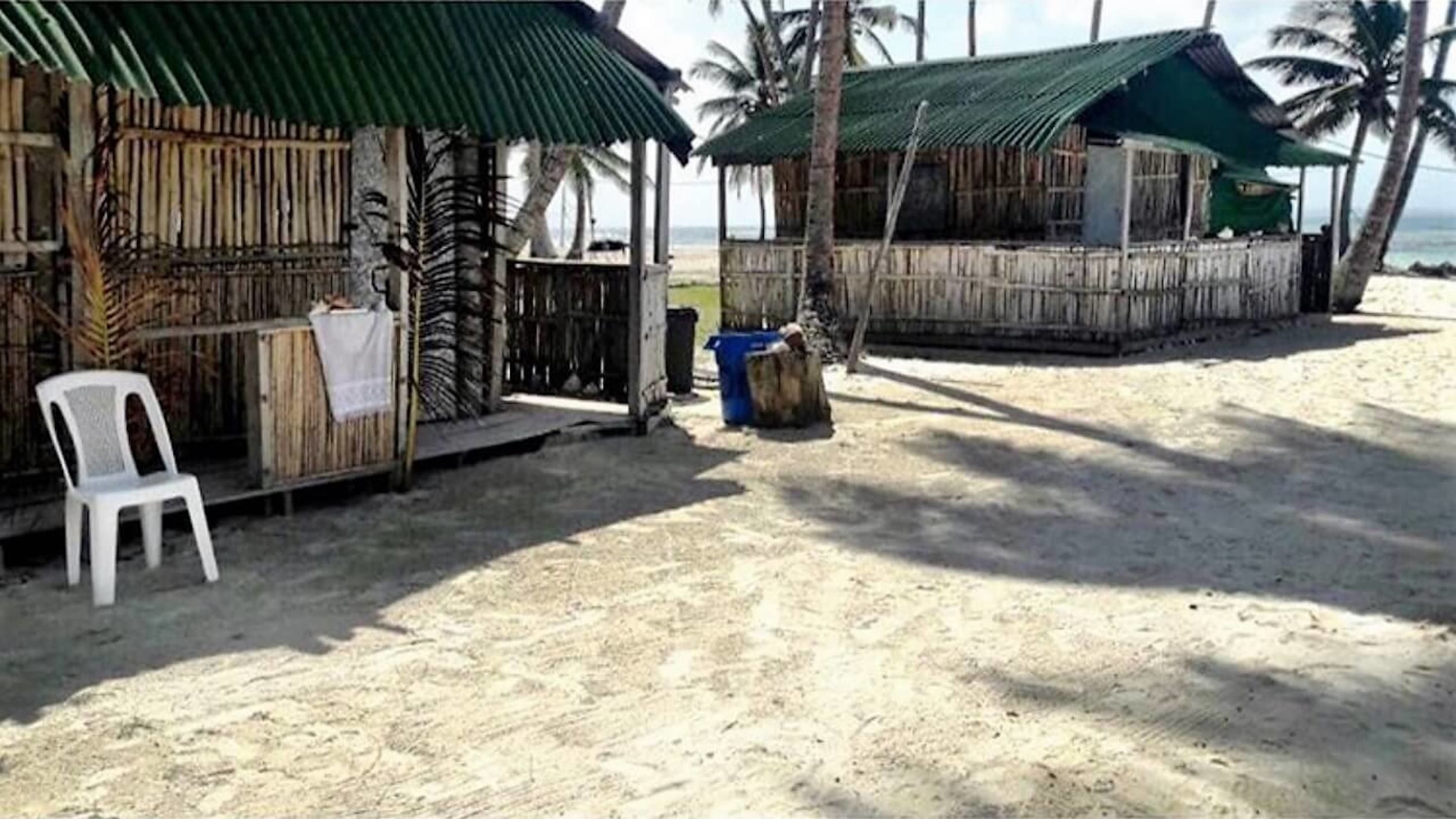 A beachside hut with a thatched roof, a white plastic chair, and a trash bin.