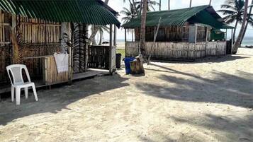 A beachside hut with a thatched roof, a white plastic chair, and a trash bin.
