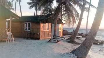 Una cabaña de playa de madera con mesa y sillas, una ventana y vistas al océano.