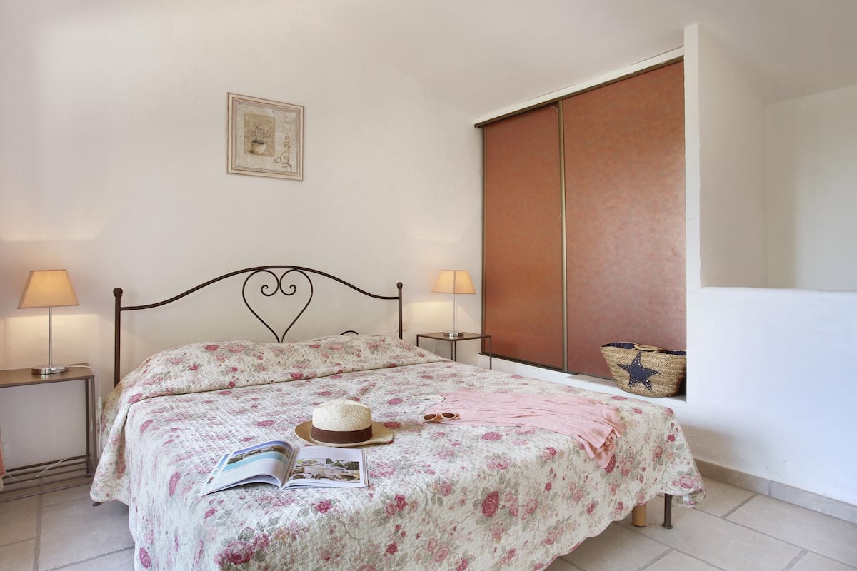 Un dormitorio con cama, dos mesitas de noche, lámpara, sombrero, libro y una cesta con estampado de estrellas.