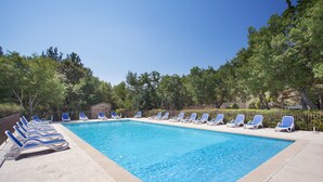 A rectangular swimming pool with a tiled edge, surrounded by a concrete deck. There are multiple blue lounge chairs aligned along the pool's edge.