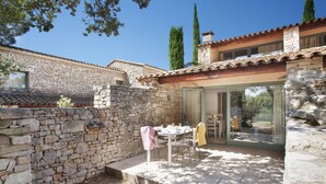 A stone-walled patio with a table and chairs, a glass door leading to a covered area, and a stone chimney.