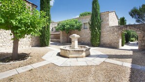 A courtyard with a stone fountain, stone walls, and a tree.