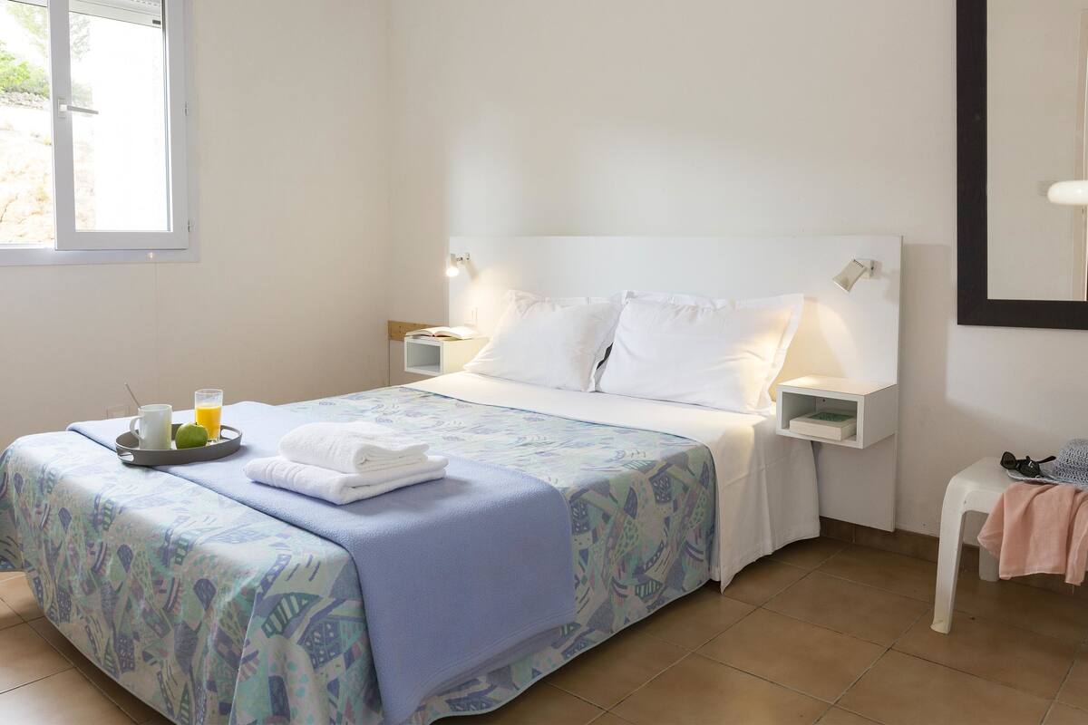 A neatly made bed with a blue patterned bedspread, white pillows, and a tray with a glass of orange juice and a white mug.