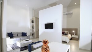 A modern hotel room with a sofa, a dining table, a bed, and a TV mounted on the wall. - Loft Mikonos - Adults Only (Pereira)
