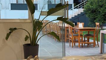 Un comedor con una mesa dispuesta para una comida, una planta en maceta y vista al exterior del edificio.