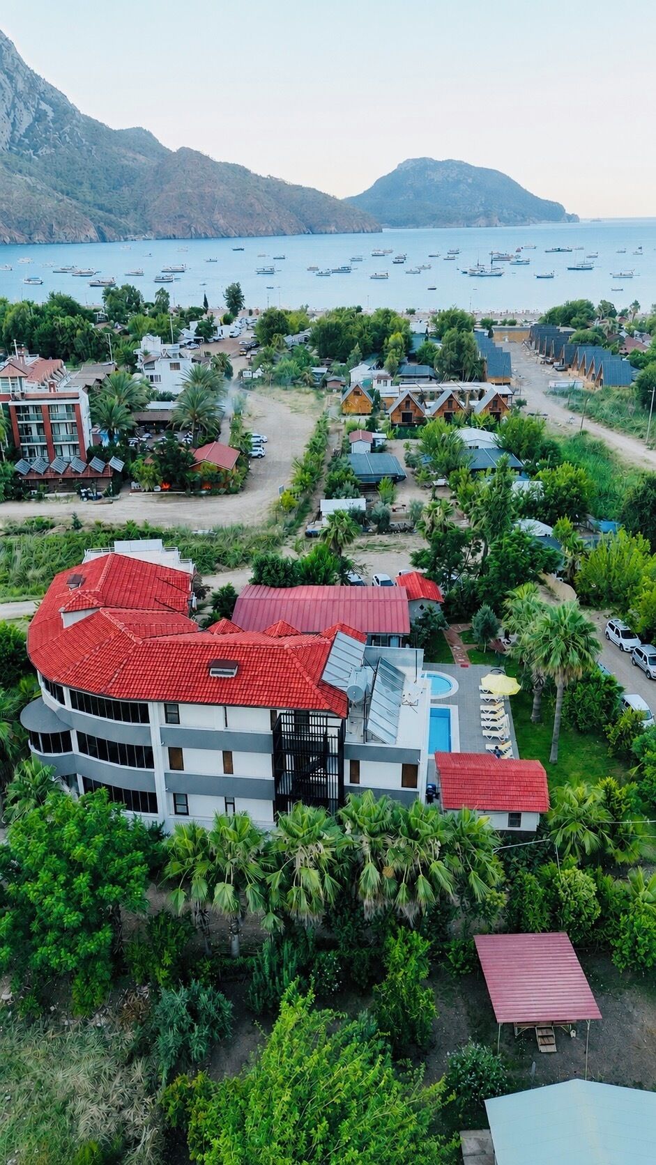 A resort with multiple buildings, a swimming pool, and a view of the sea with boats.