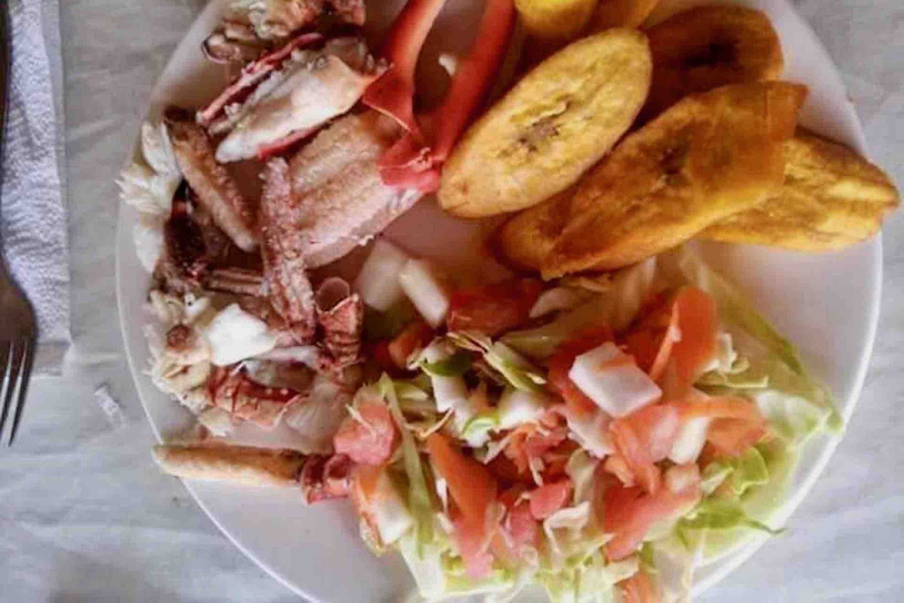 Um prato com vários alimentos, incluindo bananas fritas, uma salada e carne grelhada.