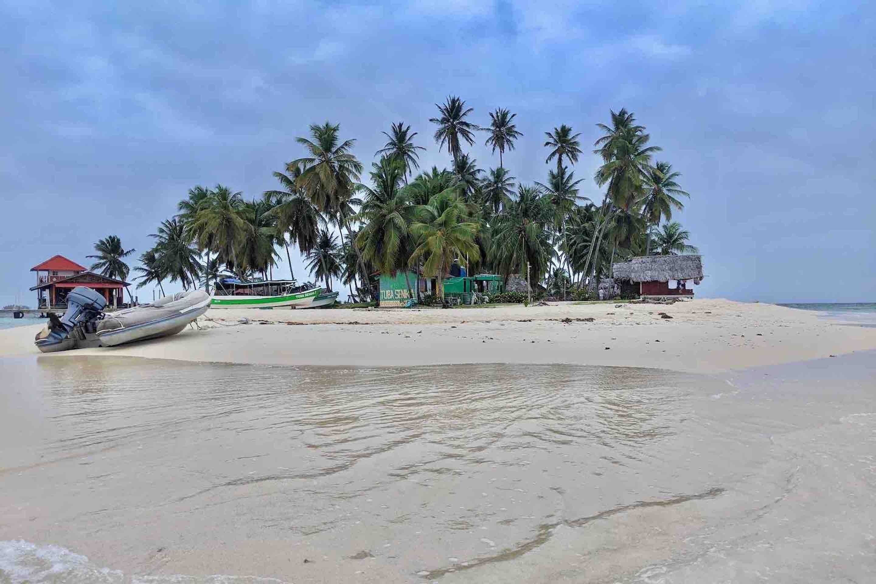 Una playa con palmeras, un bote y una pequeña cabaña.
