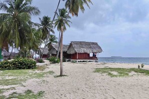 Ein Strand mit strohgedeckten Hütten, Palmen und einem Sandweg, der zum Meer führt.